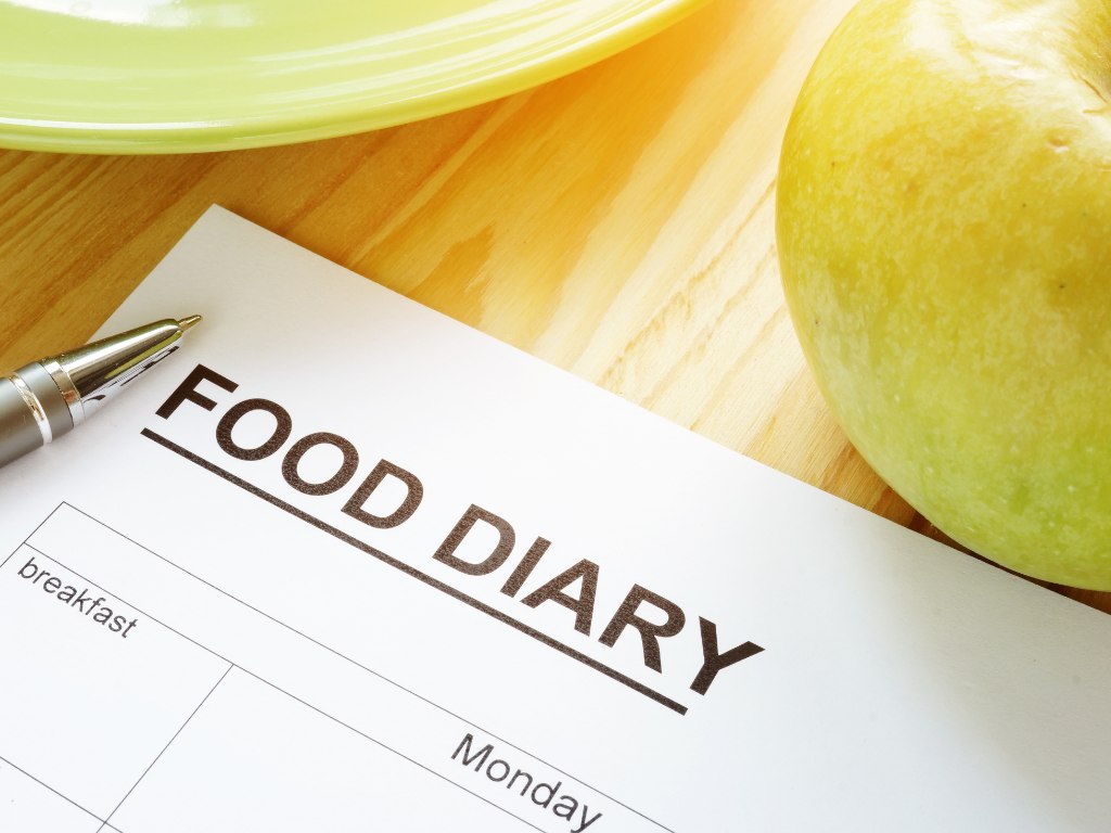 寫著 FOOD DIARY 的飲食日記表格，旁邊放著一支筆和一顆蘋果